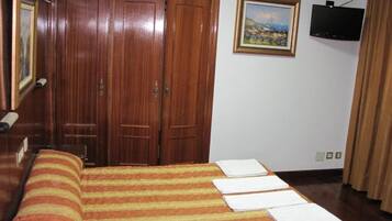 A bedroom with a bed, a wooden wardrobe, a painting on the wall, and a television.