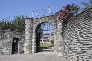 A stone archway with the word "HOTEL" above it, leading to a building with a white fence and a lawn. - Hotel Antoyana (Santander)