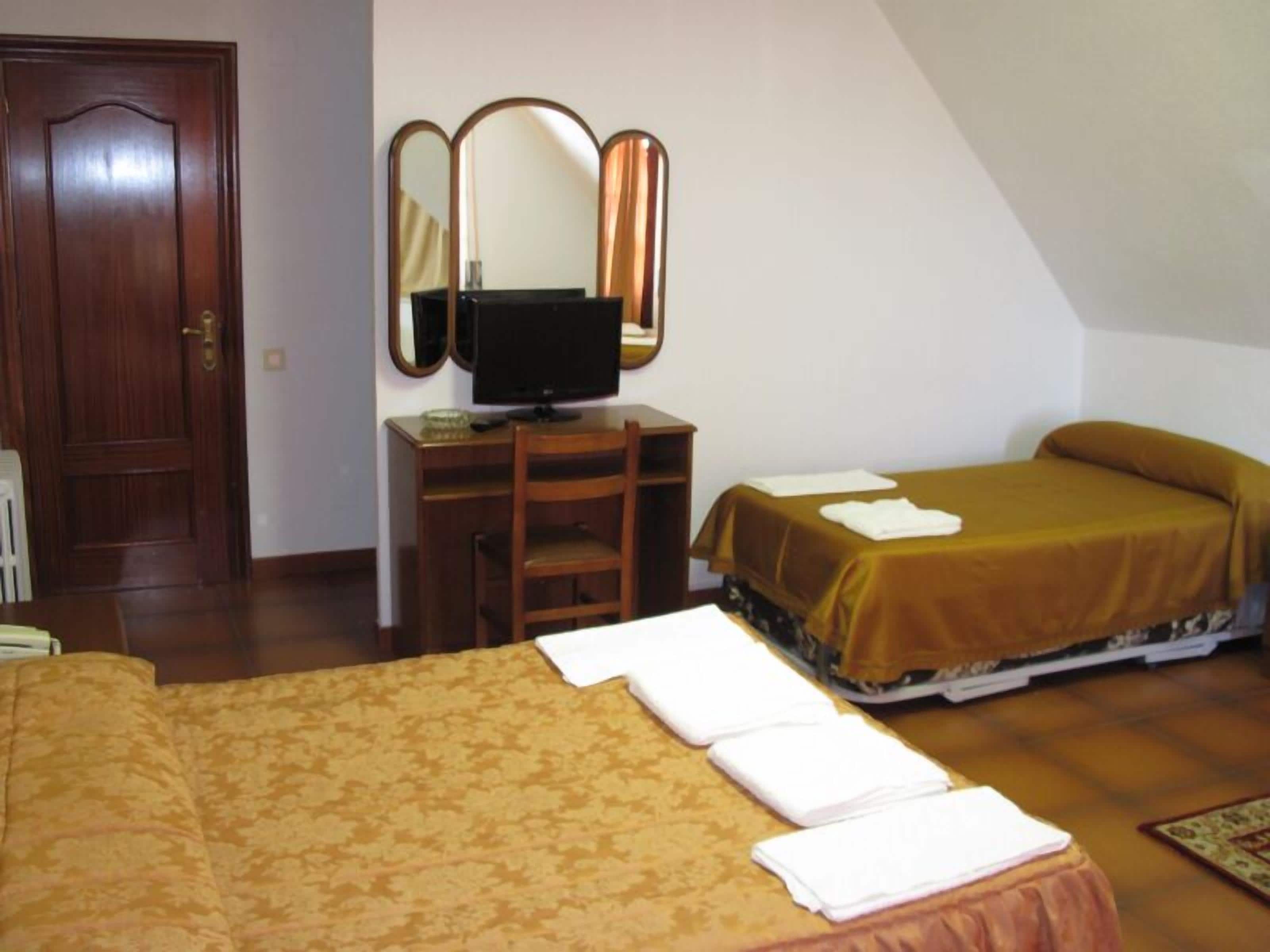 A bedroom with a bed, a desk with a computer, a chair, and a mirror.