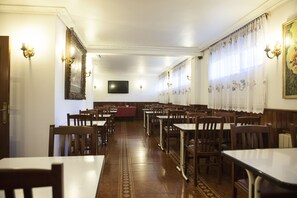 A dining area with wooden tables and chairs, a red tablecloth, and a television on the wall. - Hotel Antoyana (Santander)