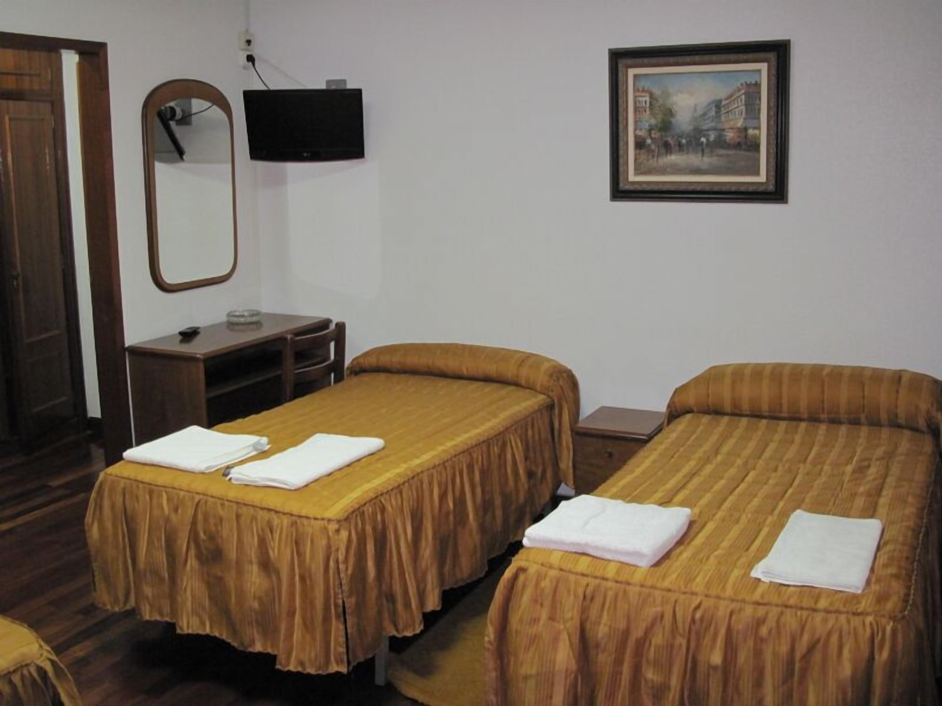 A hotel room with two single beds, a desk with a chair, a television, and a framed picture on the wall.