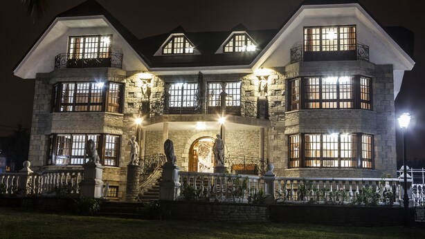 A large, multi-story house with a stone facade, multiple windows, and a balcony.