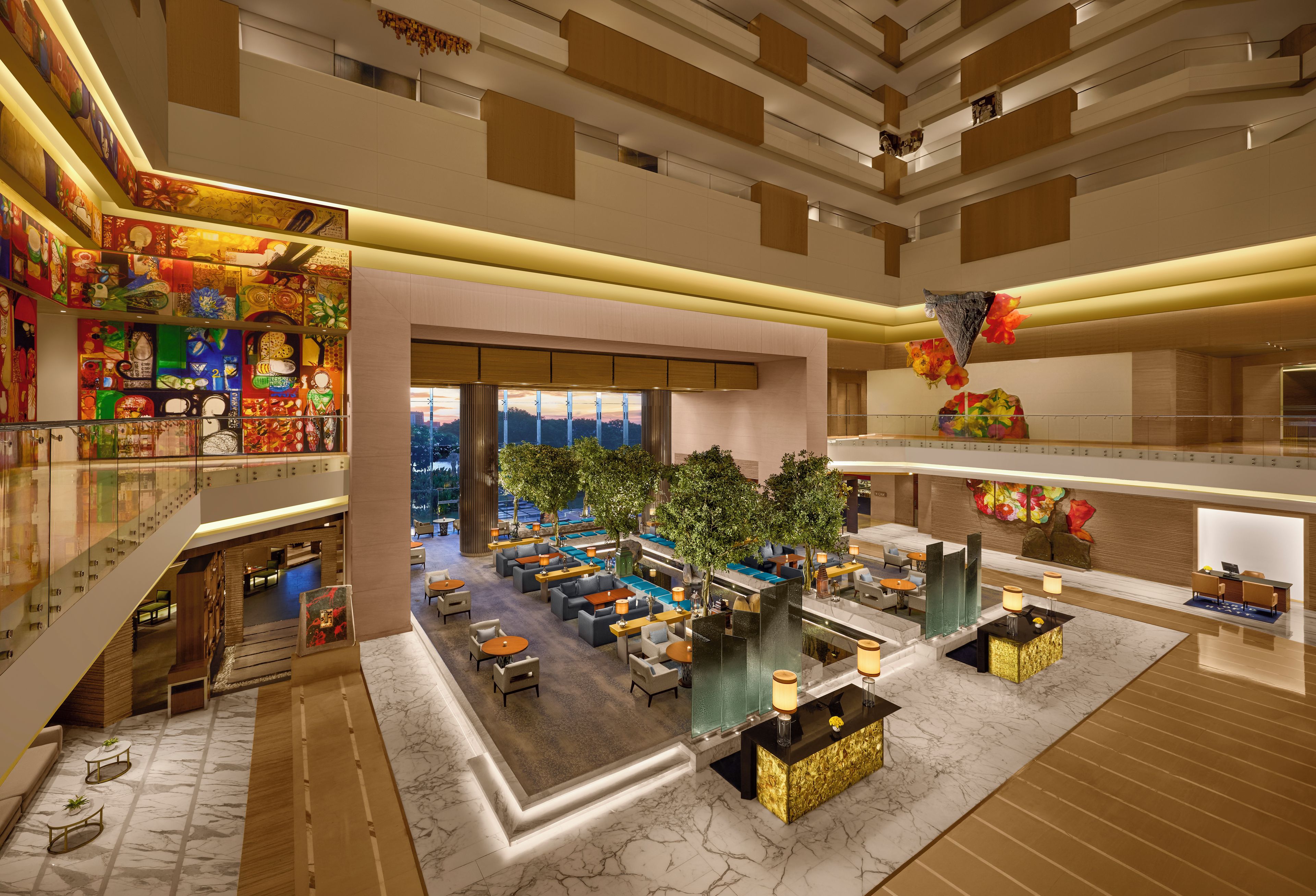 A hotel lobby with a central seating area, a staircase, and a view of the cityscape.