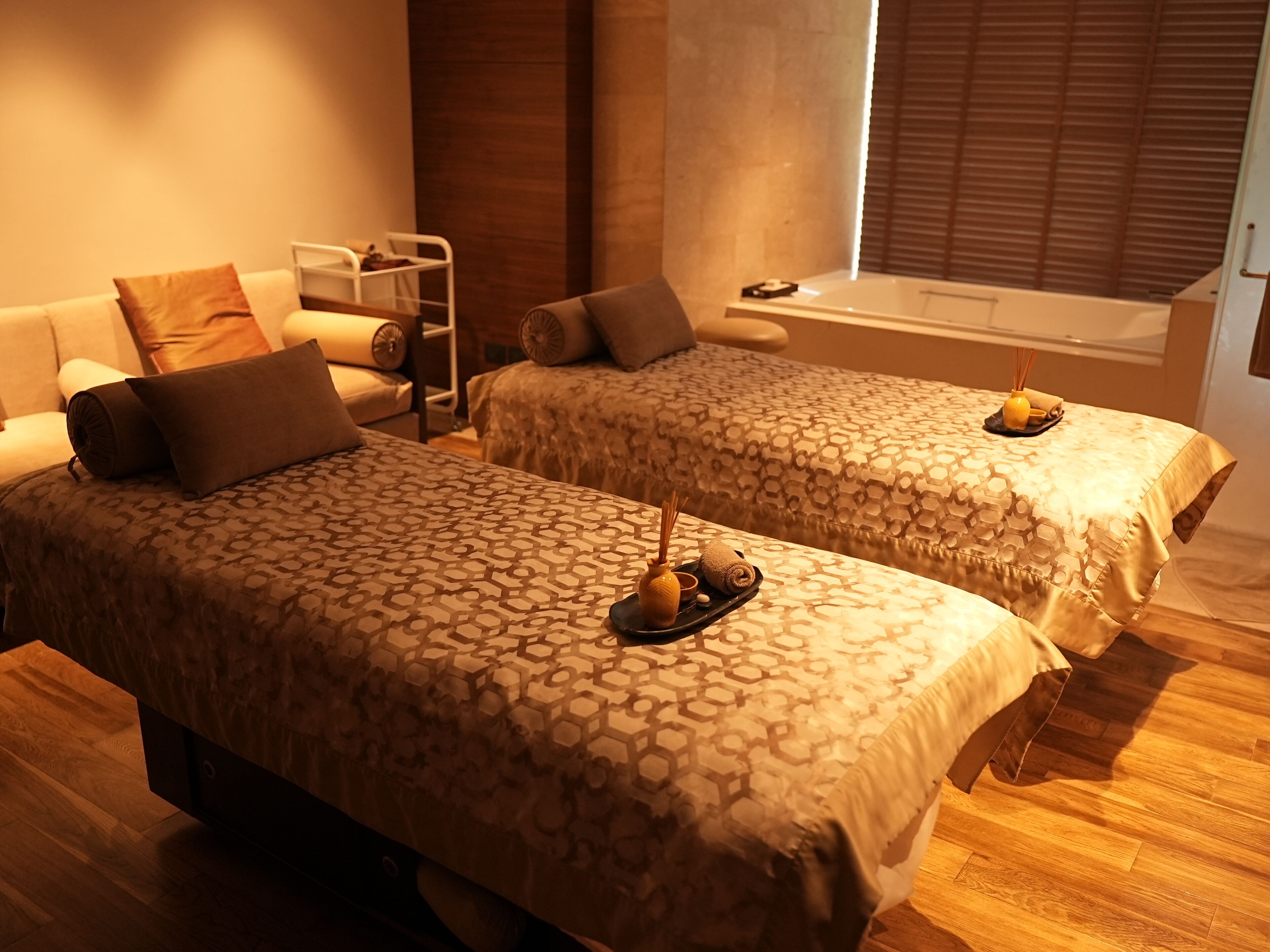 A hotel room with two beds, a sofa, a small table with a tray of amenities, and a window with blinds.