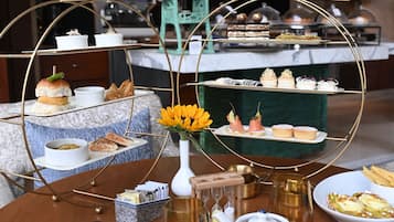 A three-tiered dessert display with various pastries and cakes, a vase with yellow flowers, and a teapot on a wooden table.