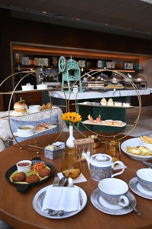A three-tiered dessert display with various pastries and cakes, a vase with yellow flowers, and a teapot on a wooden table. - Hyatt Regency Chennai (Chennai)