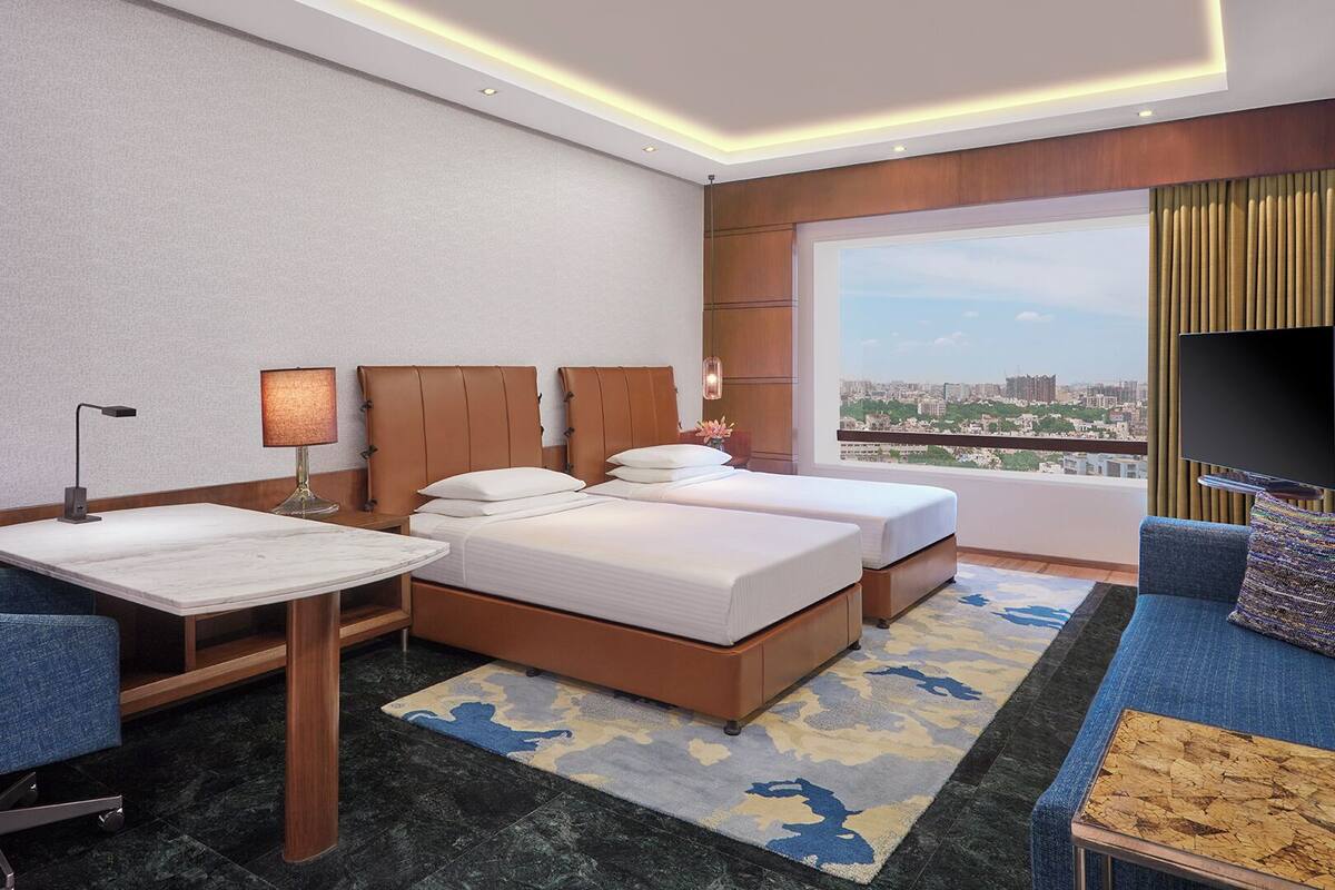 A hotel room with two beds, a desk, a chair, a sofa, a TV, and a city view.