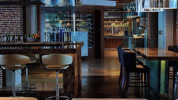 A bar area with a long counter, multiple stools, and a chandelier.
