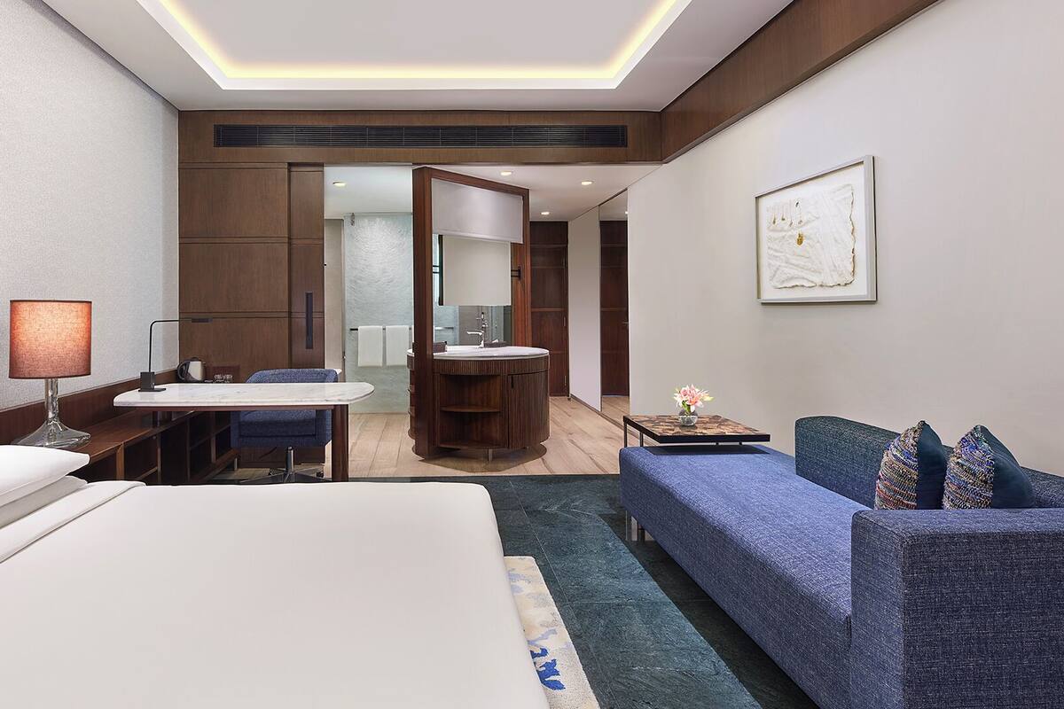 A hotel room with a bed, a desk, a sofa, and a bathroom with a mirror and sink.