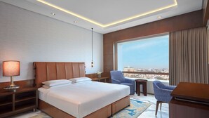 A modern hotel room with a large bed, a desk, a chair, and a view of the city.