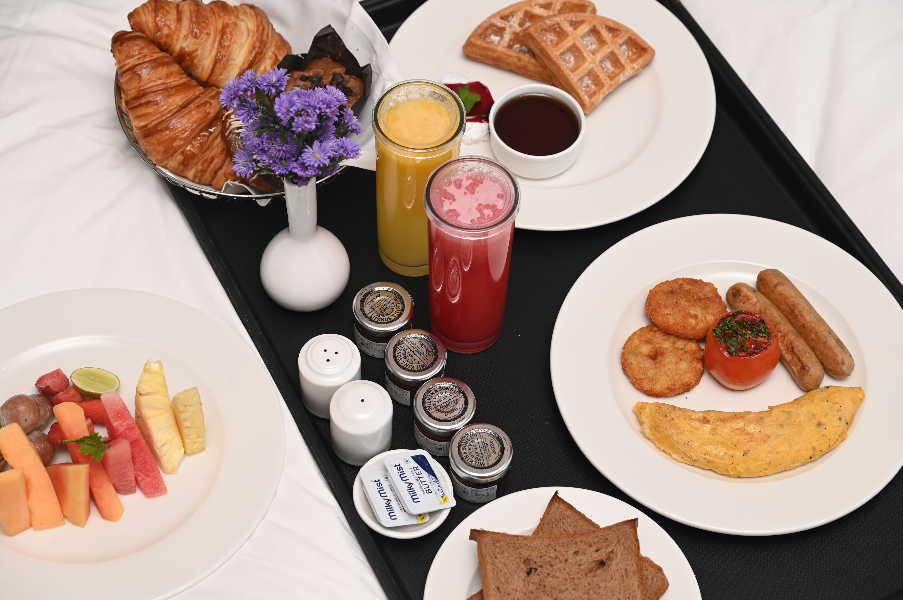 A breakfast tray with croissants, waffles, fruit, and various condiments.