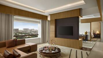 A modern living room with a large TV, comfortable seating, a round coffee table, and a view of the cityscape.