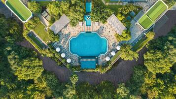 Una piscina rectangular grande rodeada por un solárium empedrado, con varias zonas de estar y árboles.