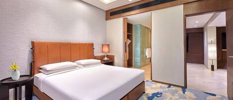 A hotel room with a large bed, a nightstand with a lamp, a vase with flowers, and a sliding door leading to a bathroom.