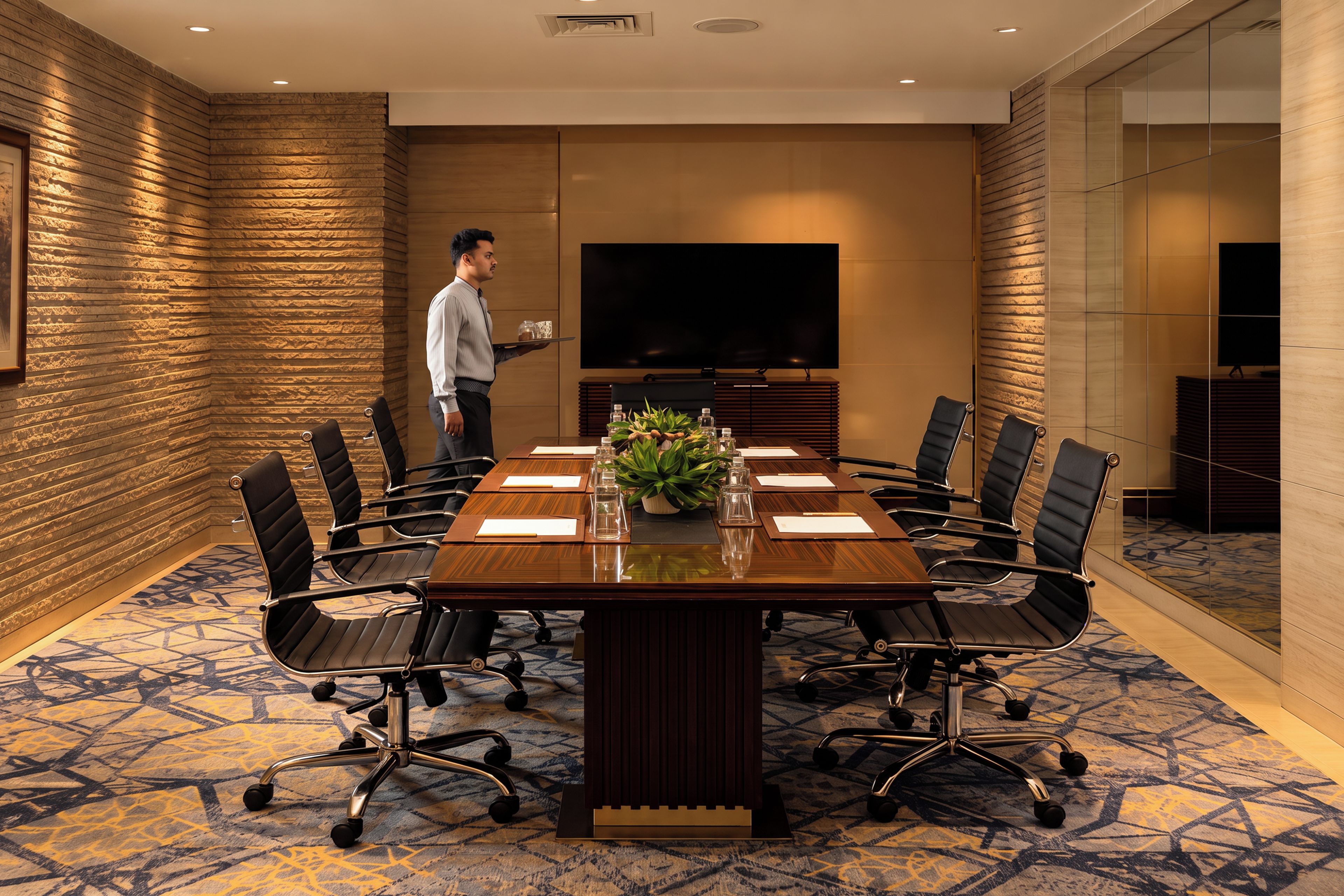 A conference room with a long table, chairs, a TV, and a person serving.