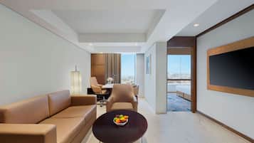 Una sala de estar moderna con un sofá, una mesa de centro con fruta, un comedor con sillas y un televisor grande en la pared.
