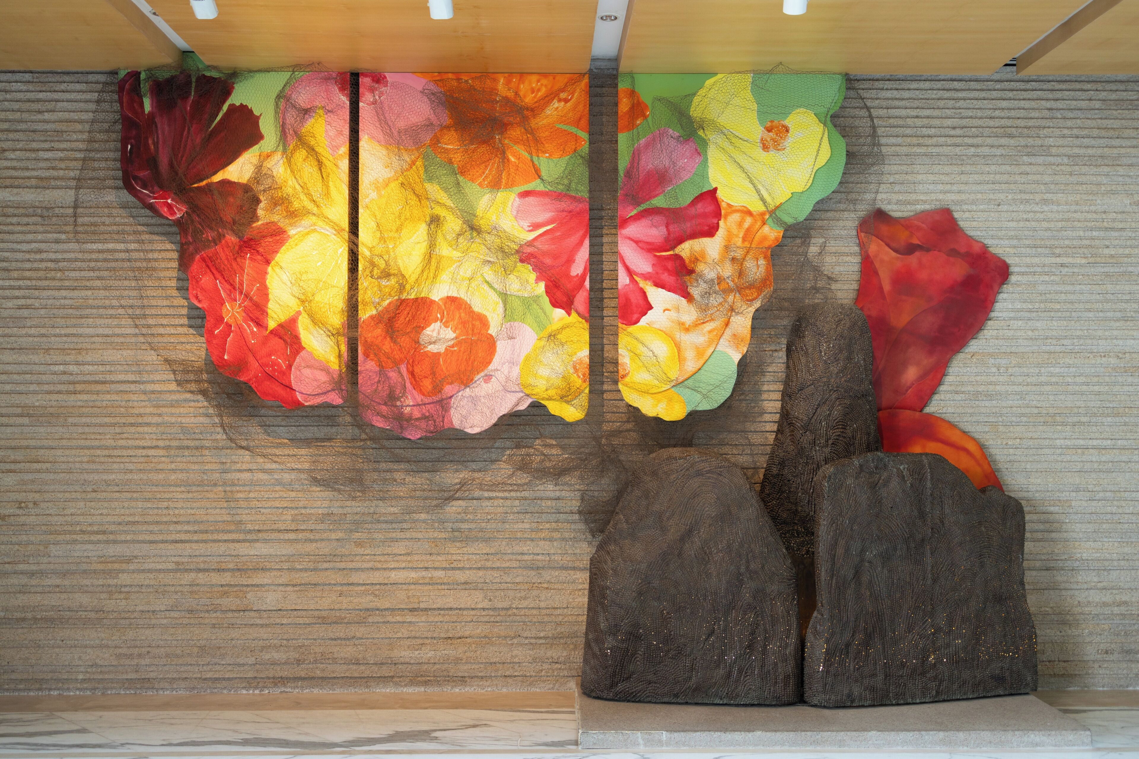 A textured wall with a floral pattern and two dark, textured sculptures.