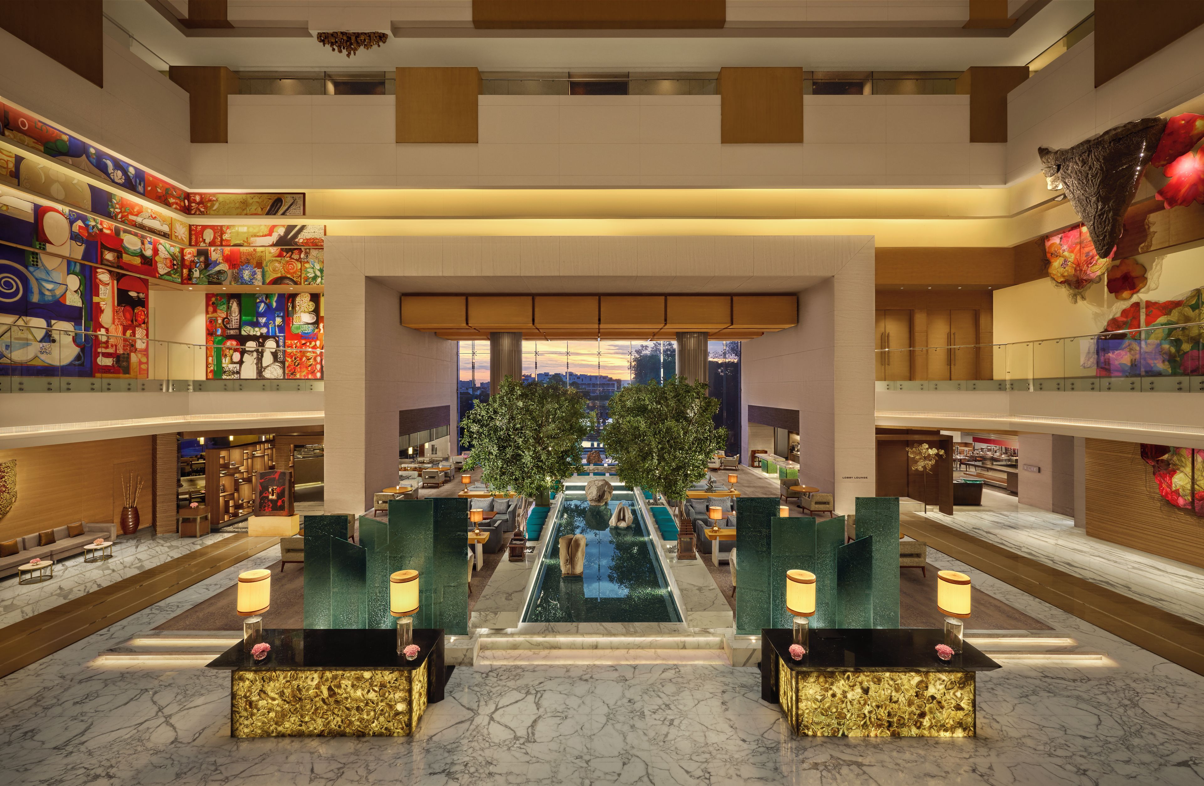 A hotel lobby with a central pool, seating areas, and a view of the cityscape.