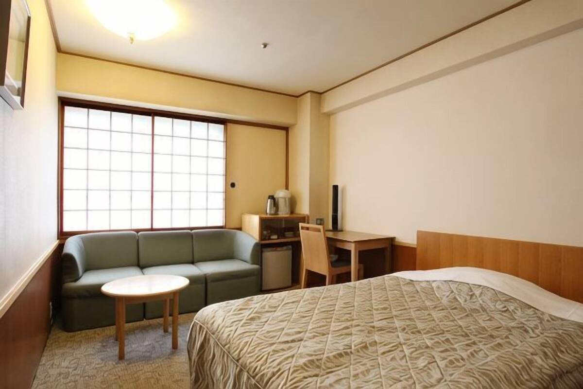 A hotel room with a bed, a sofa, a small table, a desk, and a window.