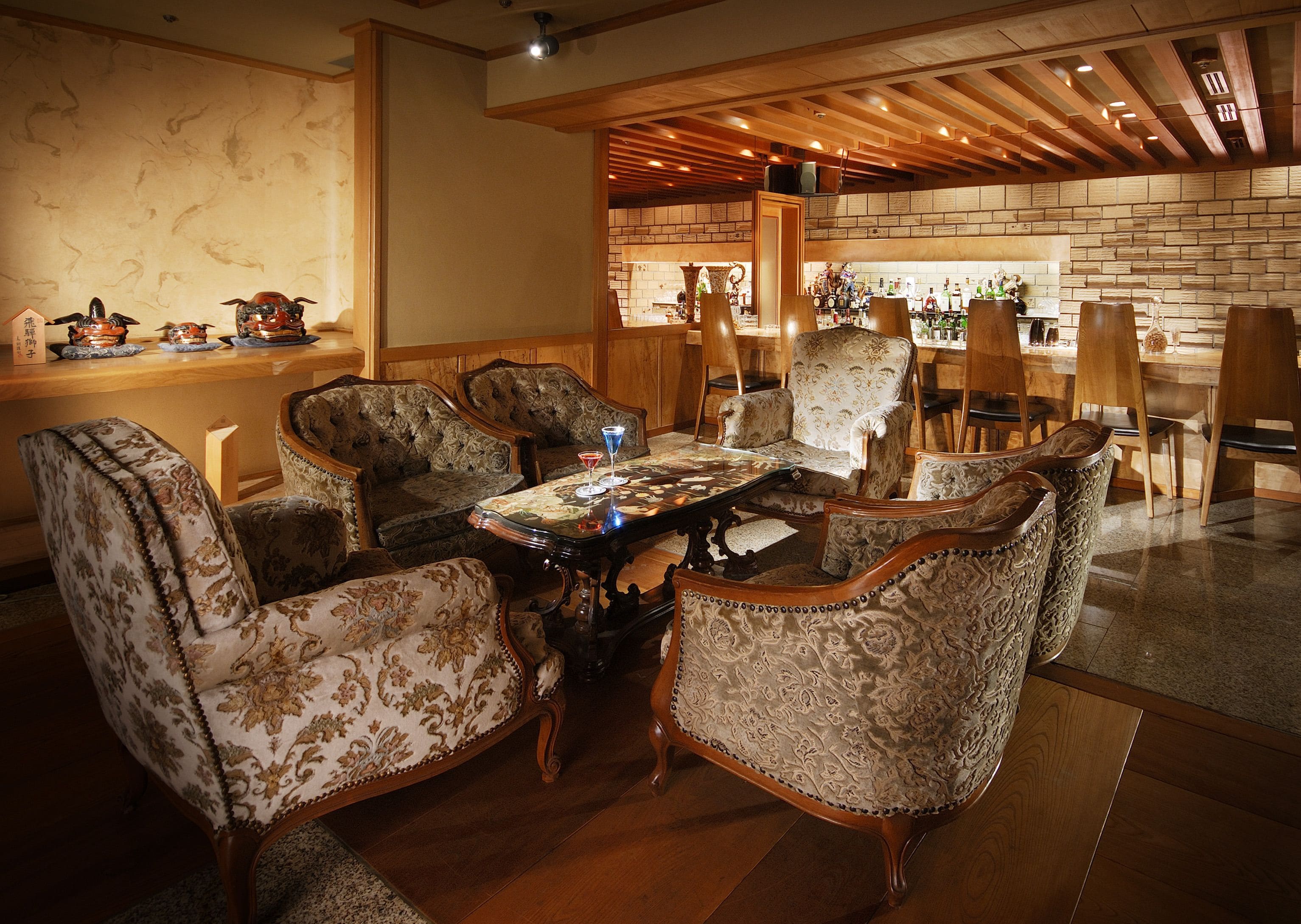 Un comedor con mesa de madera y sillas tapizadas, una zona de bar con taburetes y una pared de ladrillo.