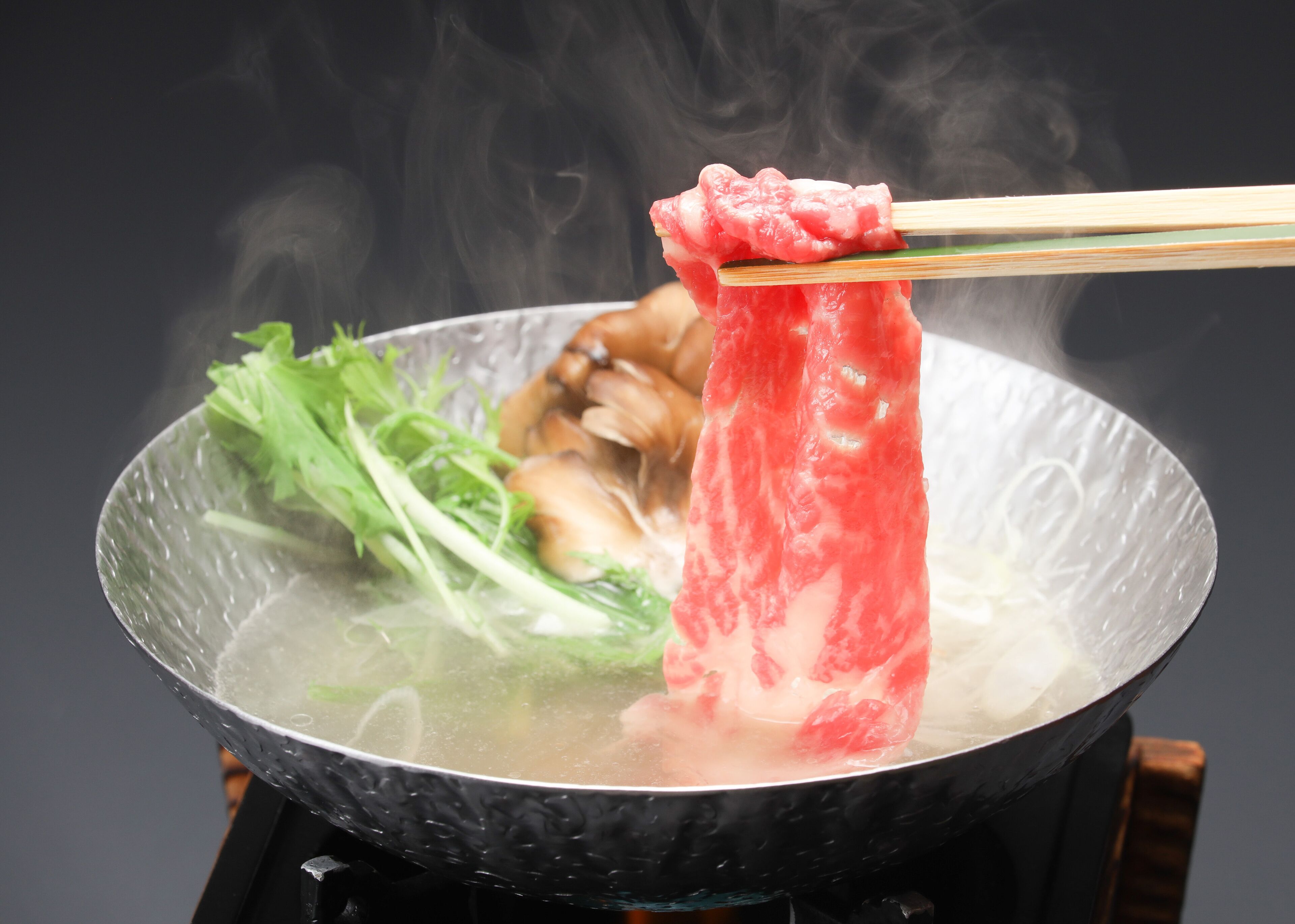 A hot pot with various ingredients, including meat and vegetables, being cooked.