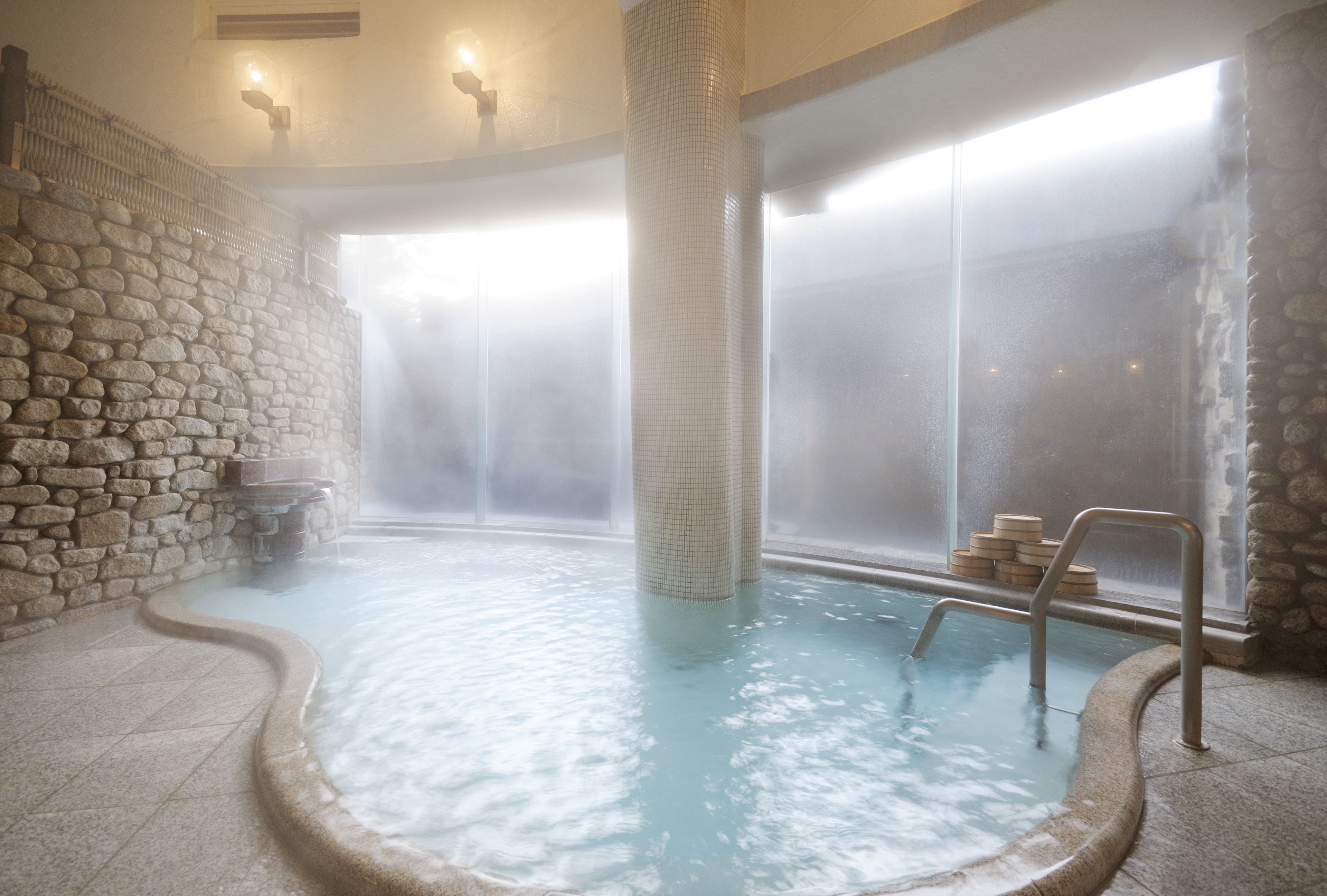 A hot spring area with stone walls, a tiled column, and a wooden bench.
