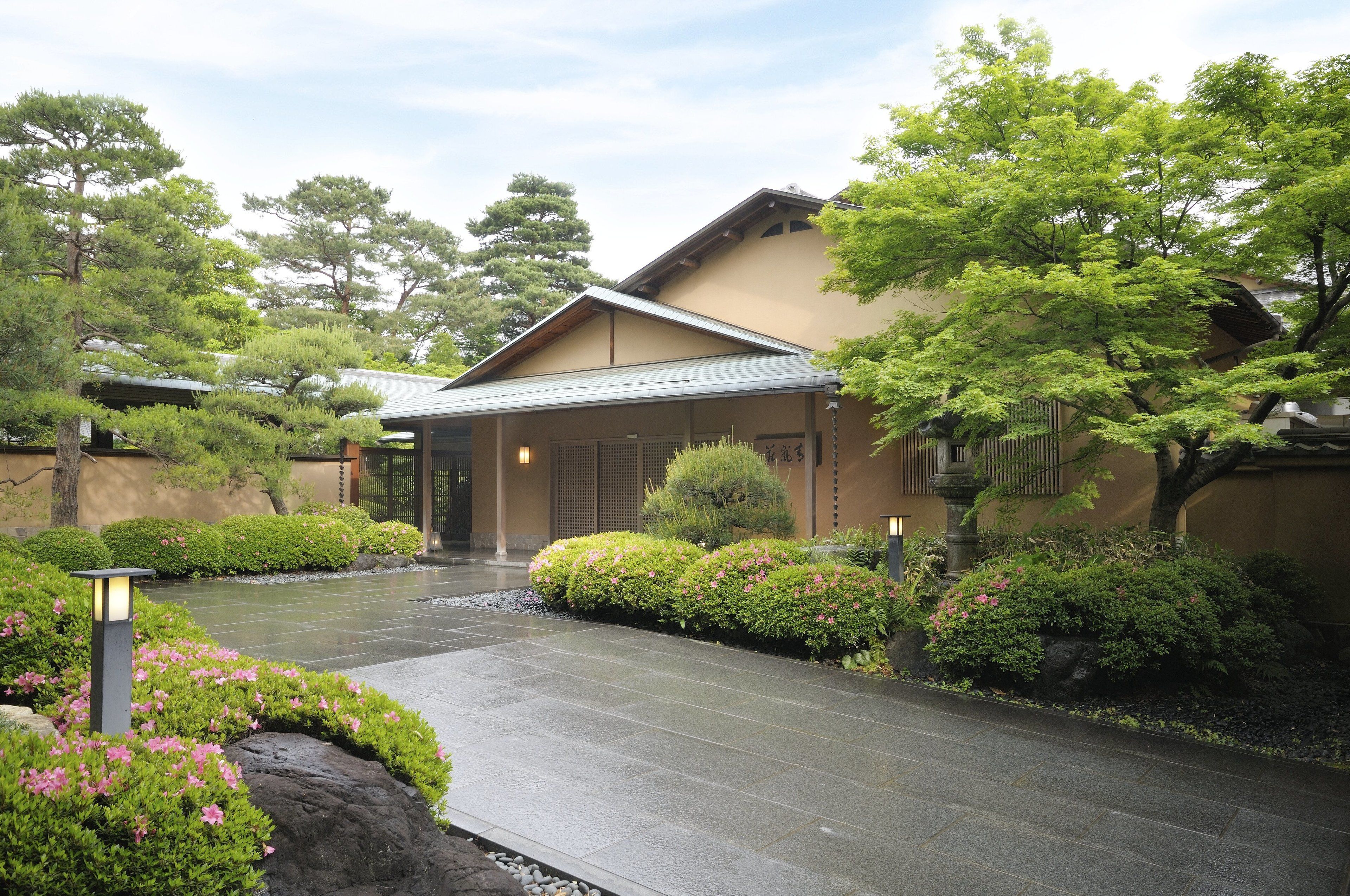 A traditional Japanese building with a tiled entrance, surrounded by well-maintained greenery and a stone pathway.