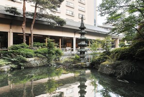 A serene courtyard with a traditional pagoda, lush greenery, and a clear pond reflecting the surroundings.