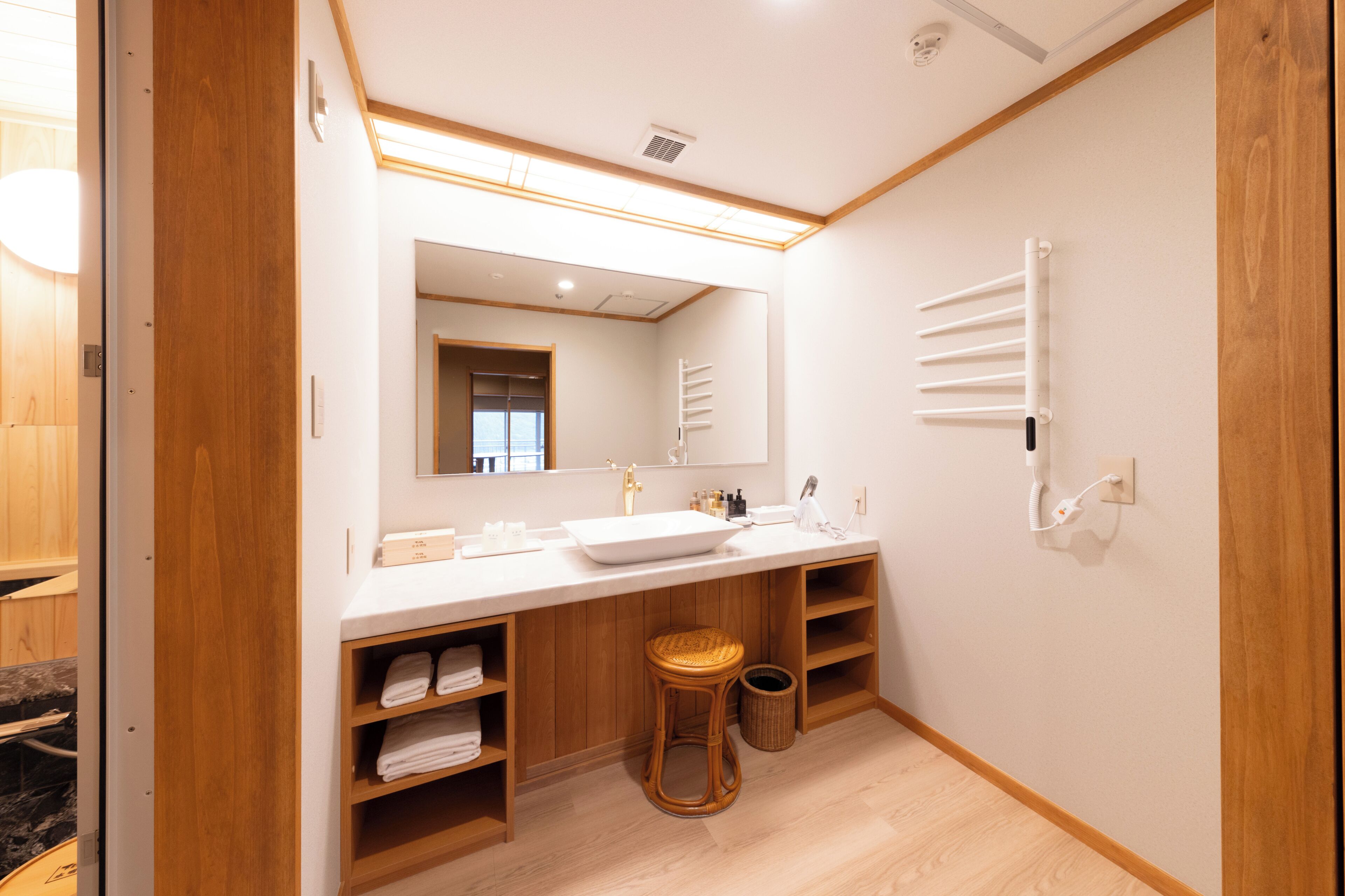 A modern bathroom with a large mirror, wooden shelves, a sink, and a towel rack.