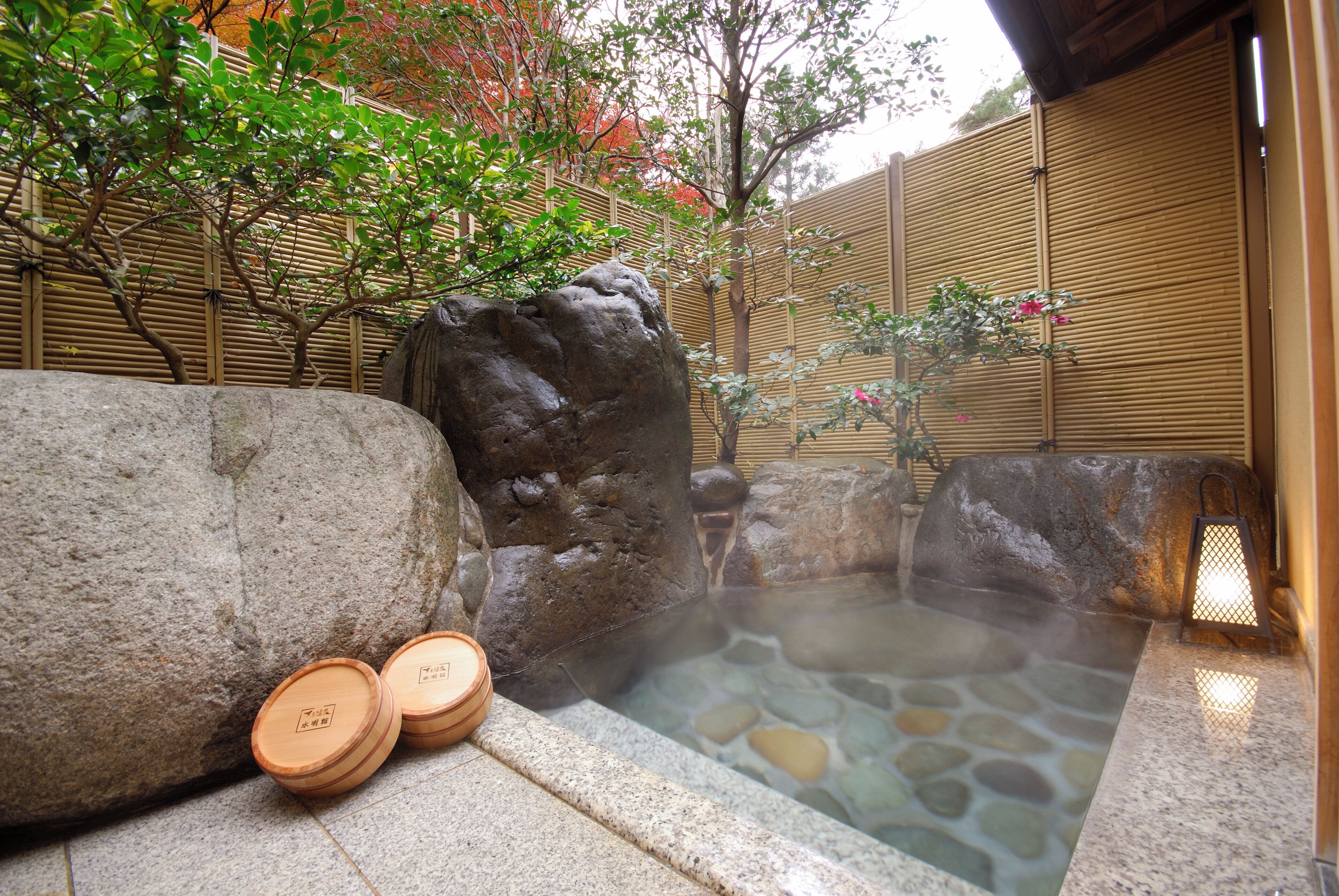 A hot spring area with stone tiles, wooden rocks, and a bamboo fence.