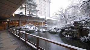 A snow-covered courtyard with a stone bridge, a small waterfall, and a traditional pagoda.