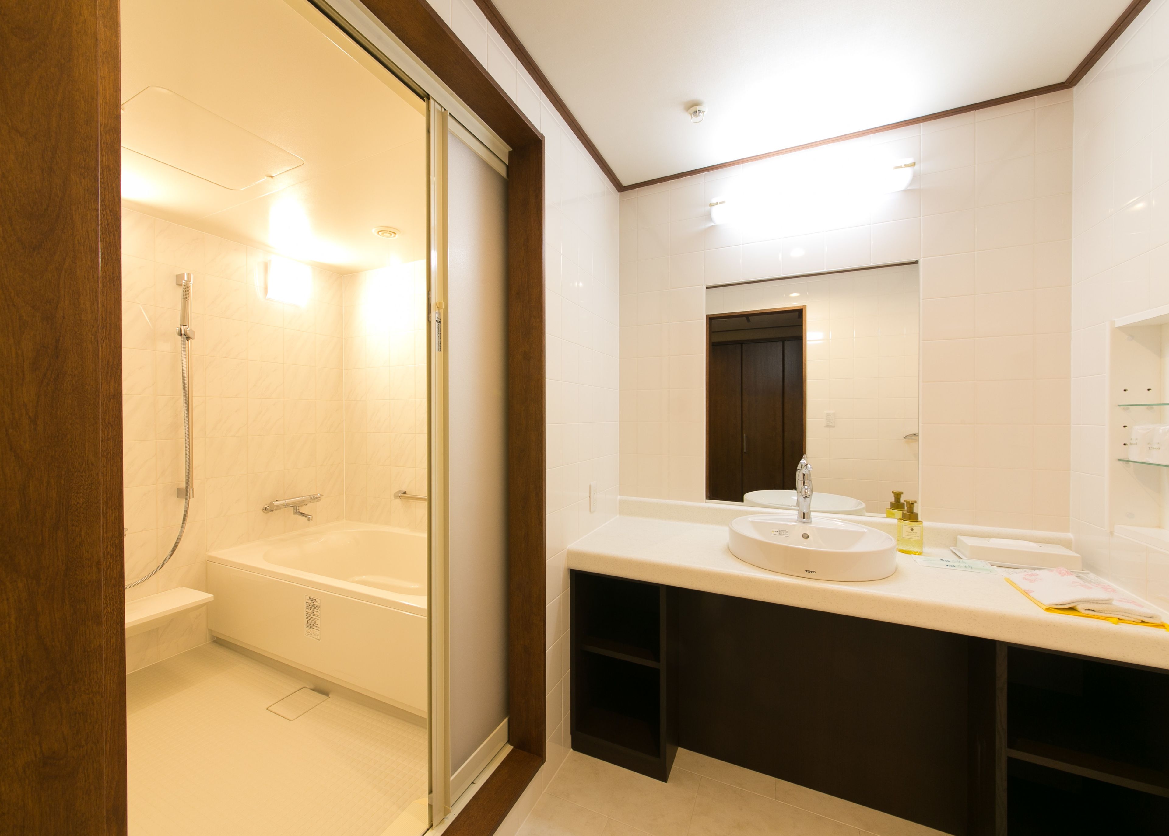 A modern bathroom with a glass-enclosed shower, a large mirror, and a vanity with a sink and toiletries.