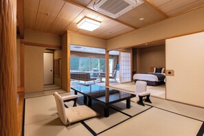 A traditional Japanese-style room with tatami flooring, a low table, a cushioned chair, and a bed with a futon.