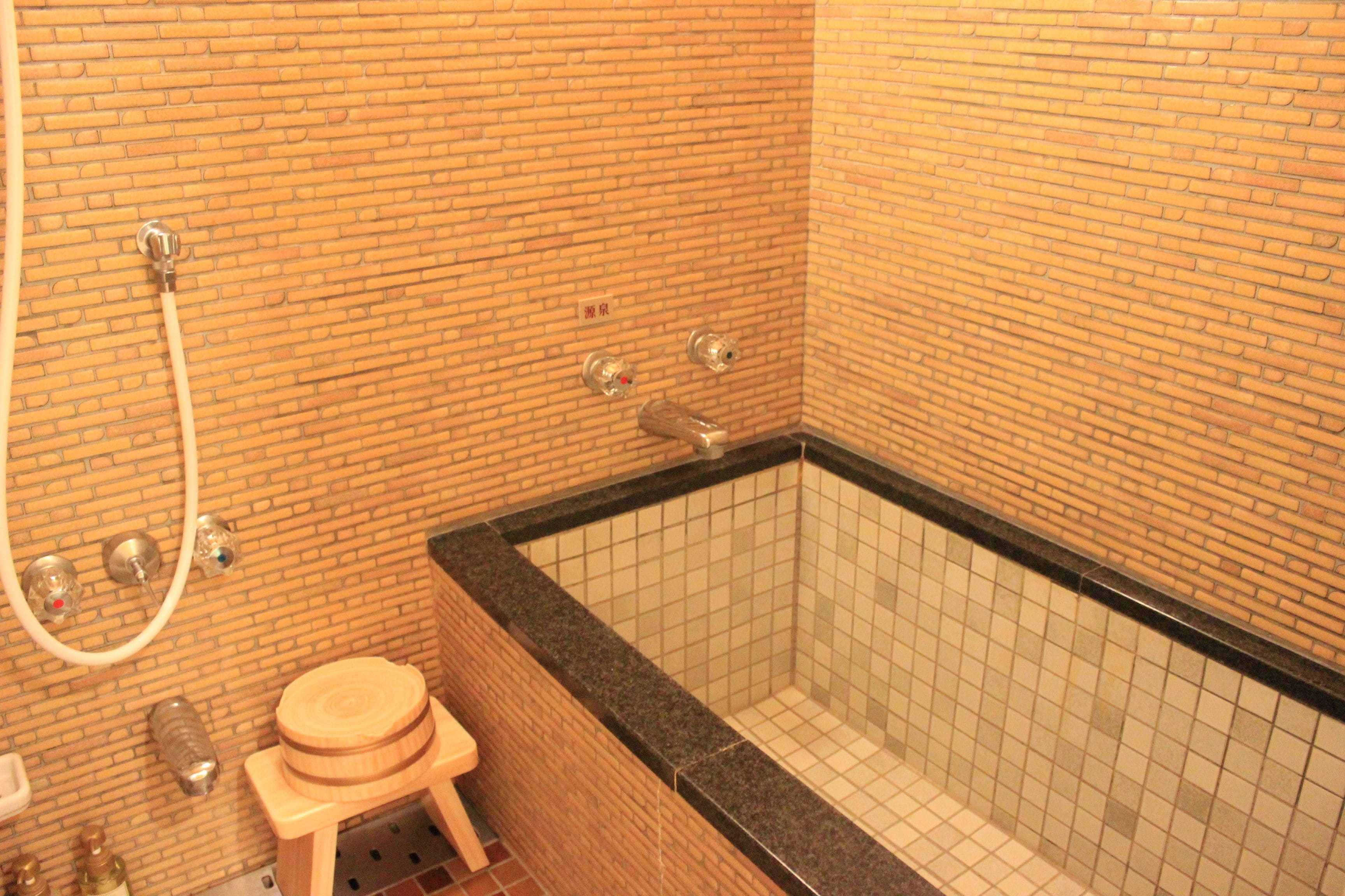 A bathroom with a brick wall, a bathtub, and a wooden stool.