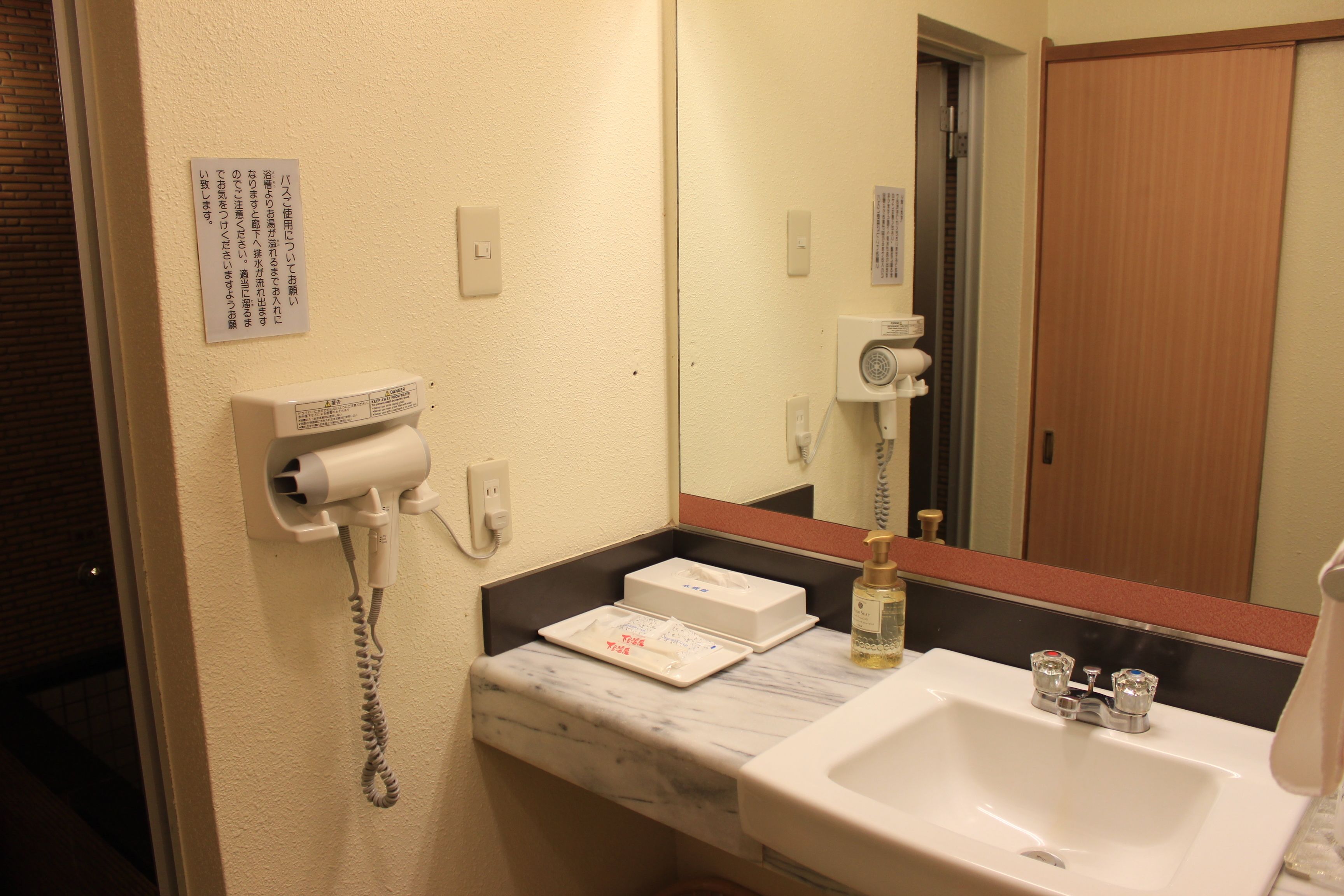Une salle de bain équipée d’un lavabo, d’un miroir, d’un sèche-cheveux et d’un distributeur de serviettes.
