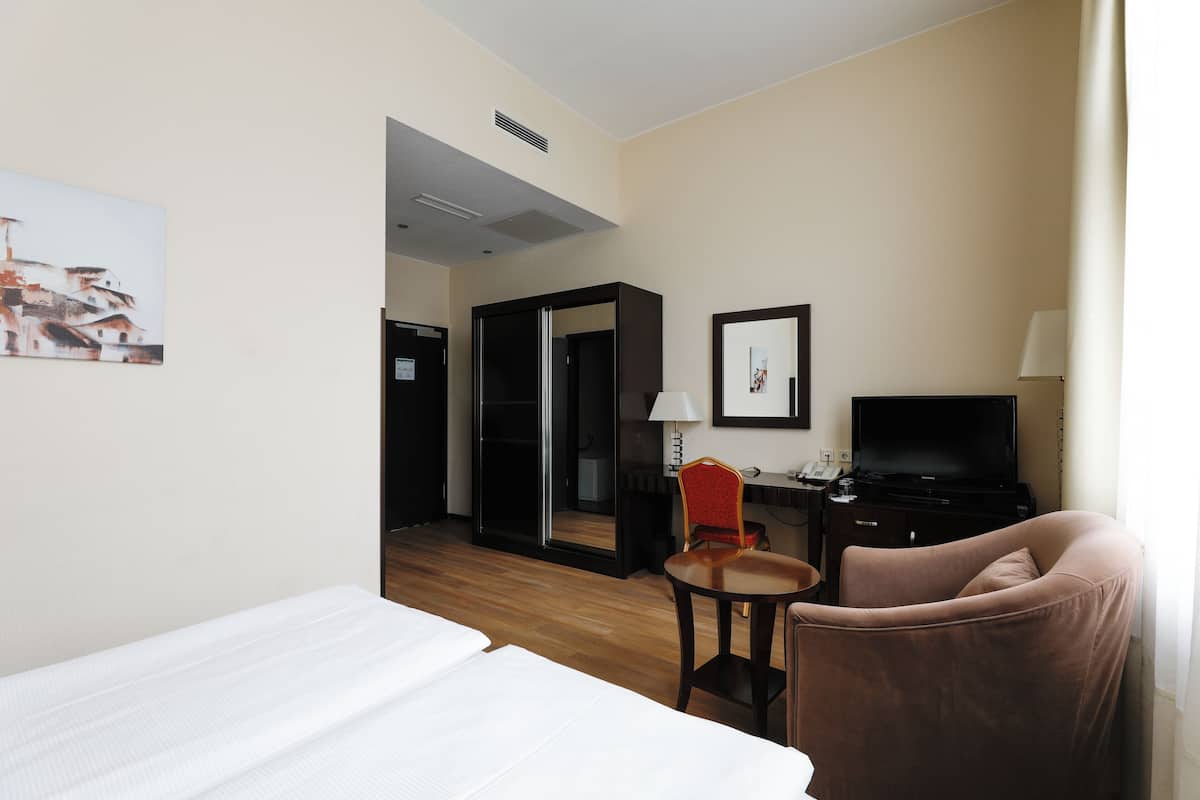Quarto de hotel com cama, escrivaninha, computador, televisão e cadeira.
