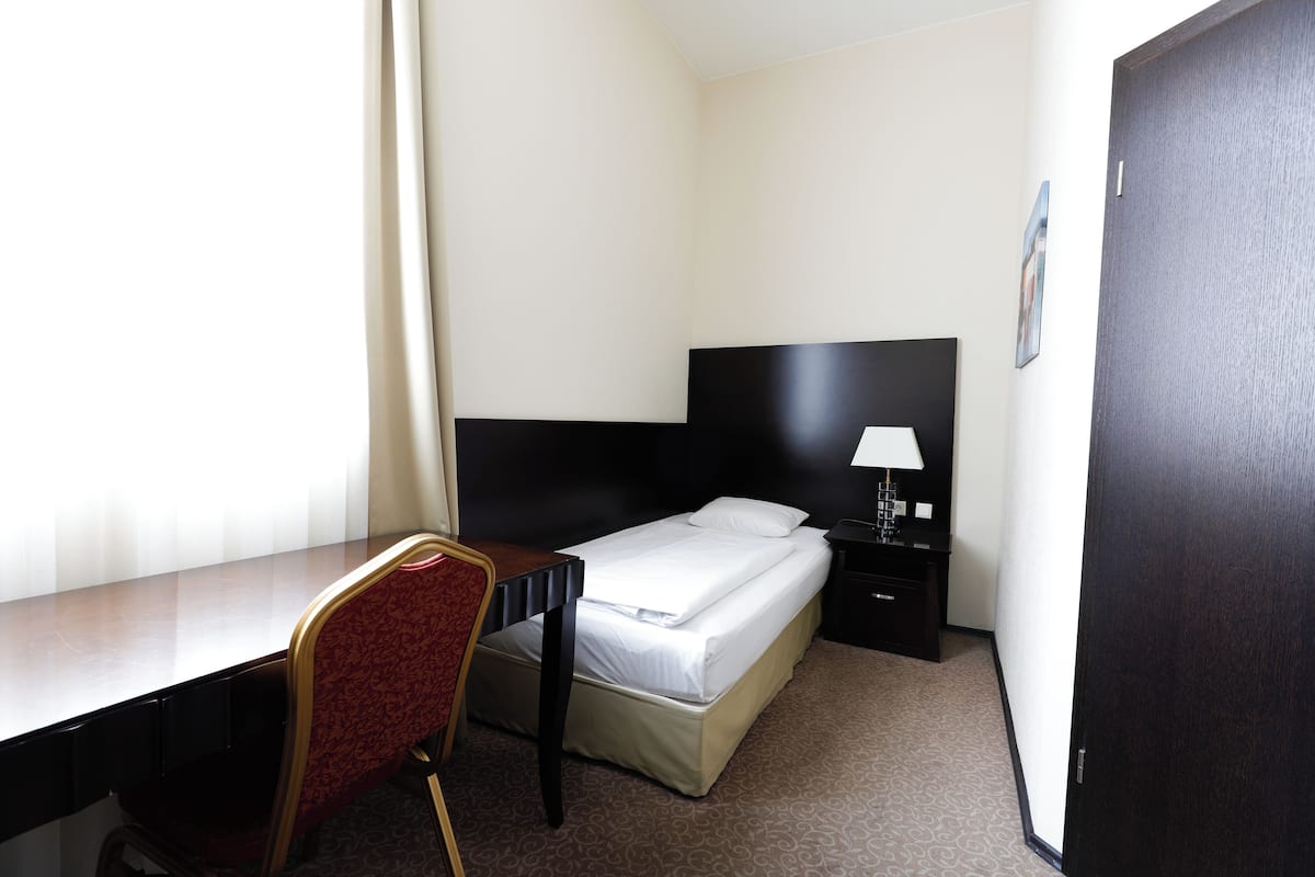 Quarto de hotel com cama, escrivaninha, cadeira, mesa de cabeceira e porta.