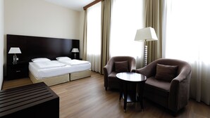 Une chambre d’hôtel comprenant un lit, deux tables de chevet, un bureau, deux fauteuils et une lampe.