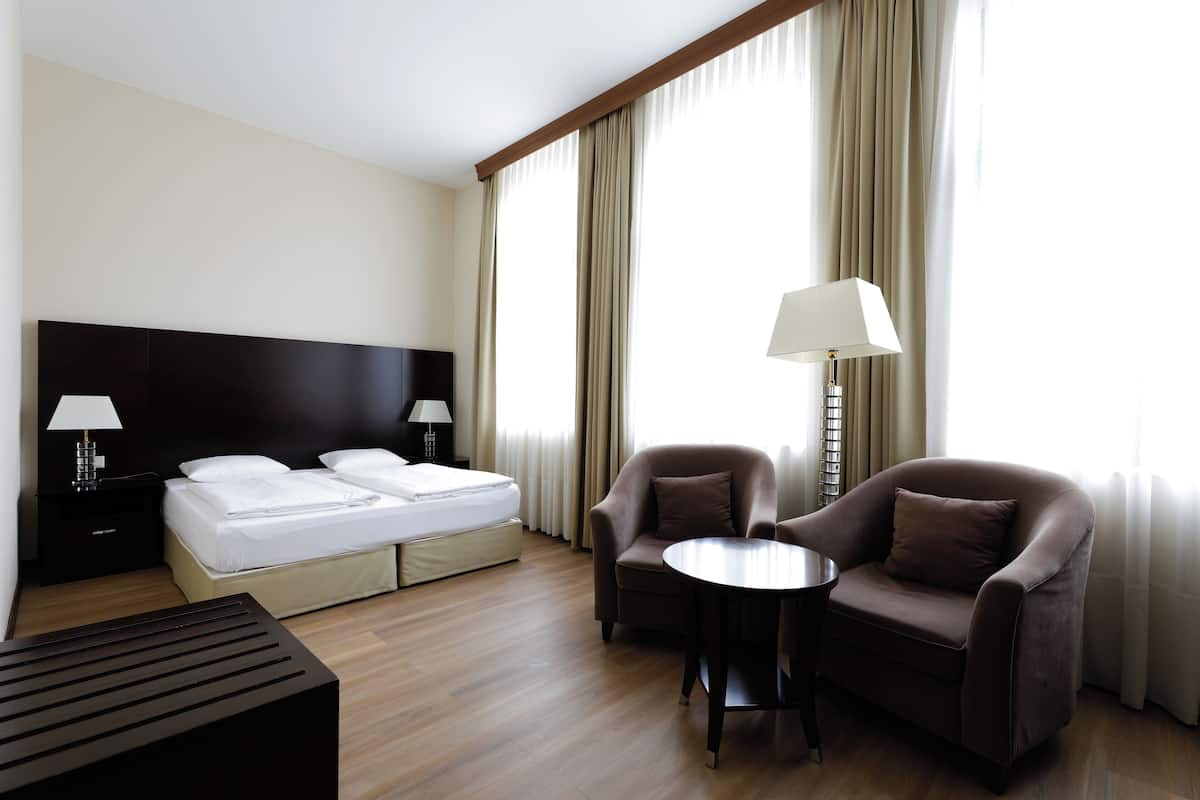 Quarto de hotel com cama, duas mesas de cabeceira, escrivaninha, duas poltronas e luminária.