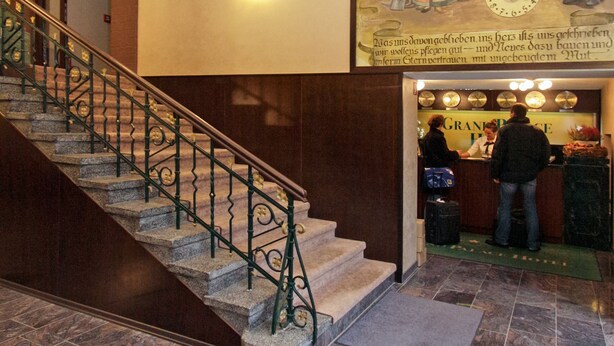 Un grand escalier orné d’une rampe en métal mène à un espace d’accueil où est accrochée une grande peinture au mur.