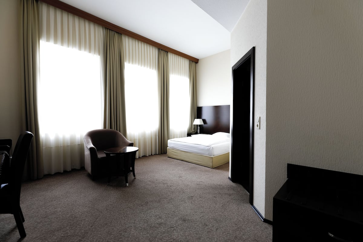 Quarto de hotel com uma cama, uma cadeira, uma escrivaninha e uma televisão.