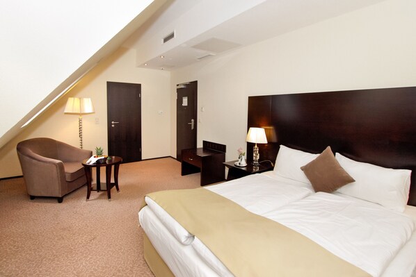 Una habitación de hotel con una cama, una silla, un escritorio y una lámpara.