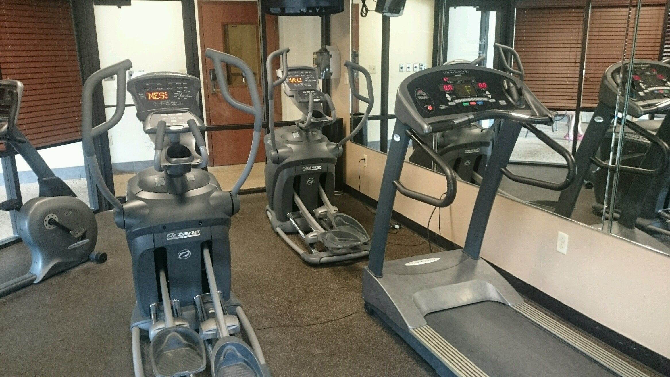Ein Fitnessraum mit Laufbändern, Crosstrainern und Fahrrädern.