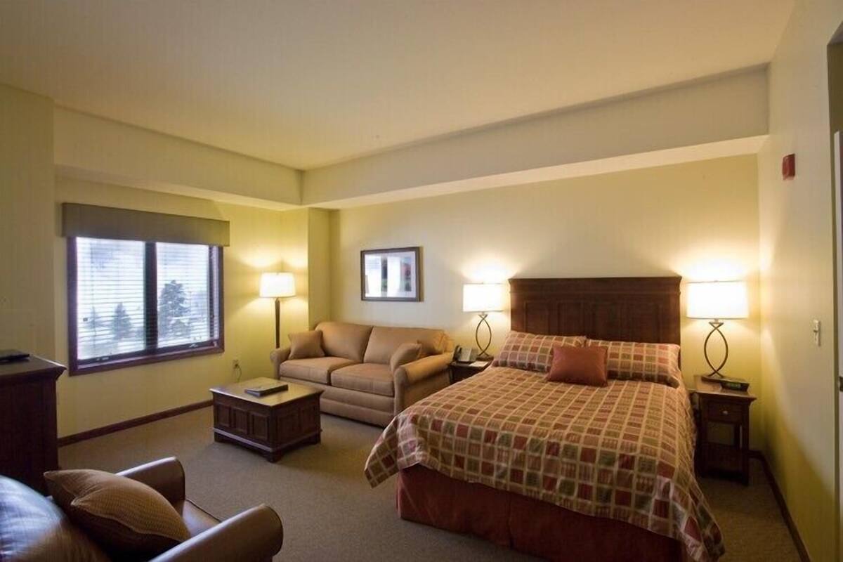 Ein Hotelzimmer mit einem Bett, zwei Nachttischen, einem Sofa, einem Sessel, einem Schreibtisch und einem Fenster.