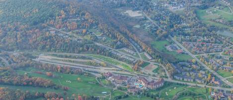 An aerial view of a golf course with a clubhouse, roads, and surrounding greenery.