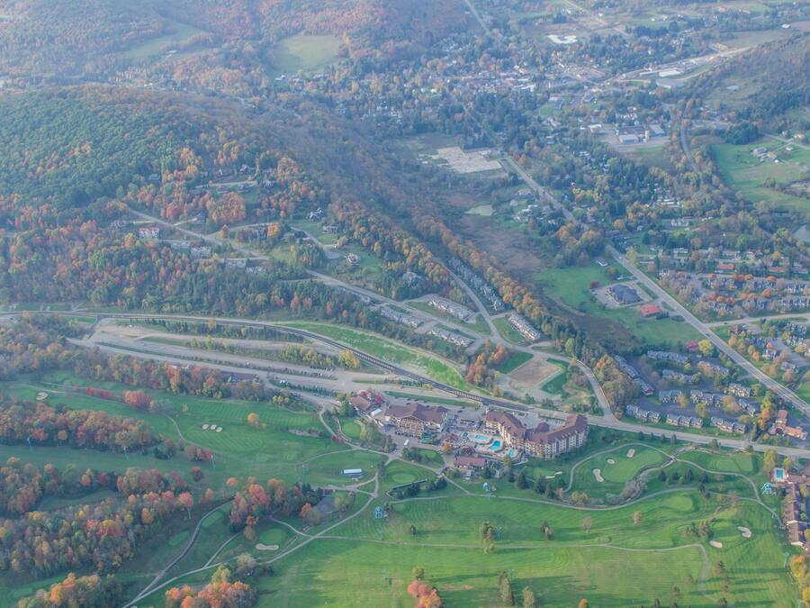 An aerial view of a golf course with a clubhouse, roads, and surrounding greenery.