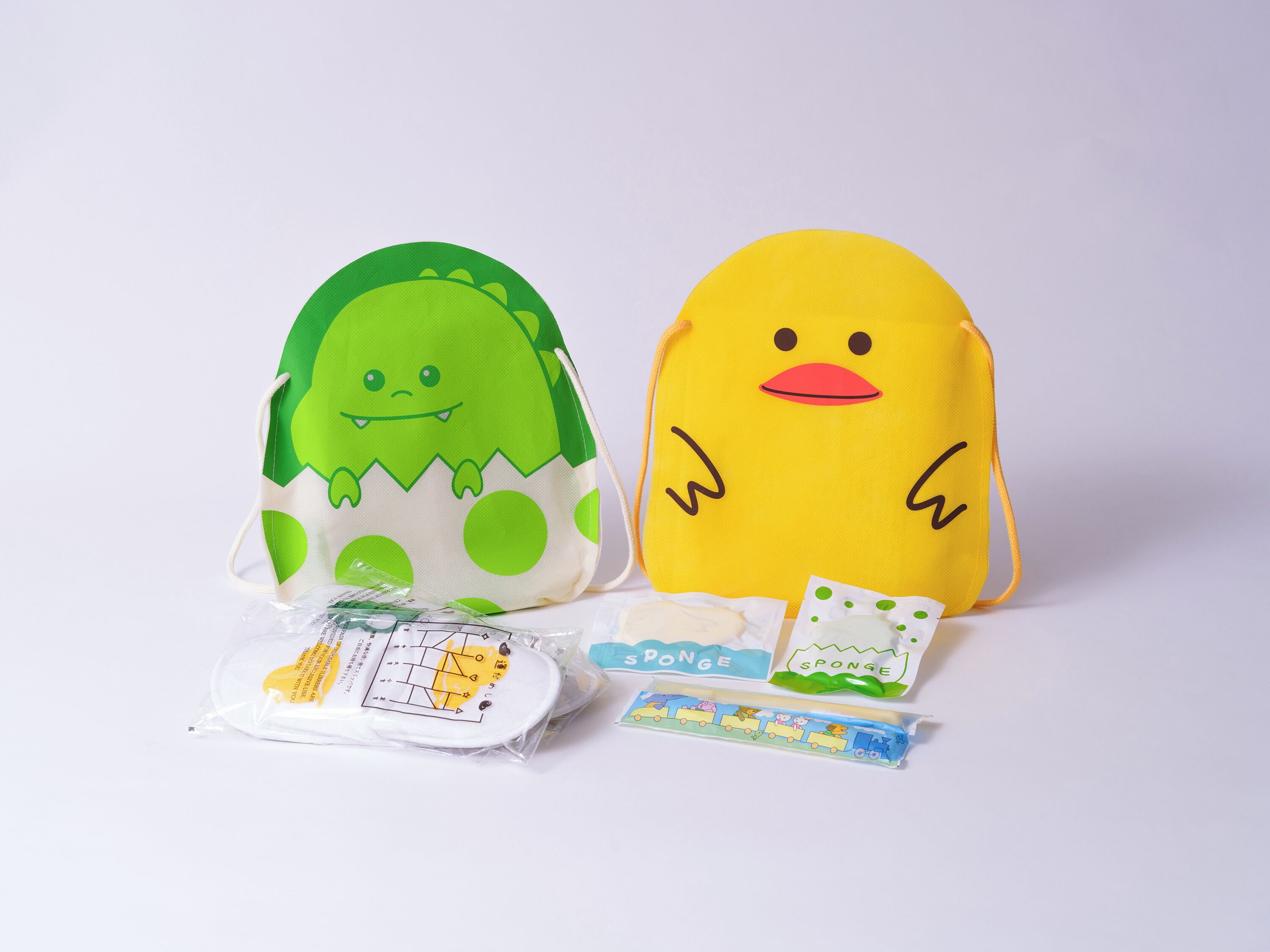 Two plush toys, one green and one yellow, with a small package and a toy train set in front.