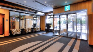 A hotel lobby with a reception desk, seating area, and glass doors leading outside. - APA Hotel Kitakami Ekinishi (Kitakami)