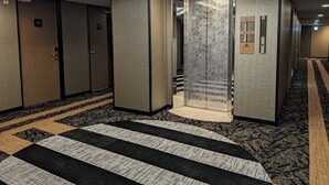 A hotel corridor with a carpeted floor, a glass elevator, and a door marked with the number 707. - APA Hotel Kitakami Ekinishi (Kitakami)