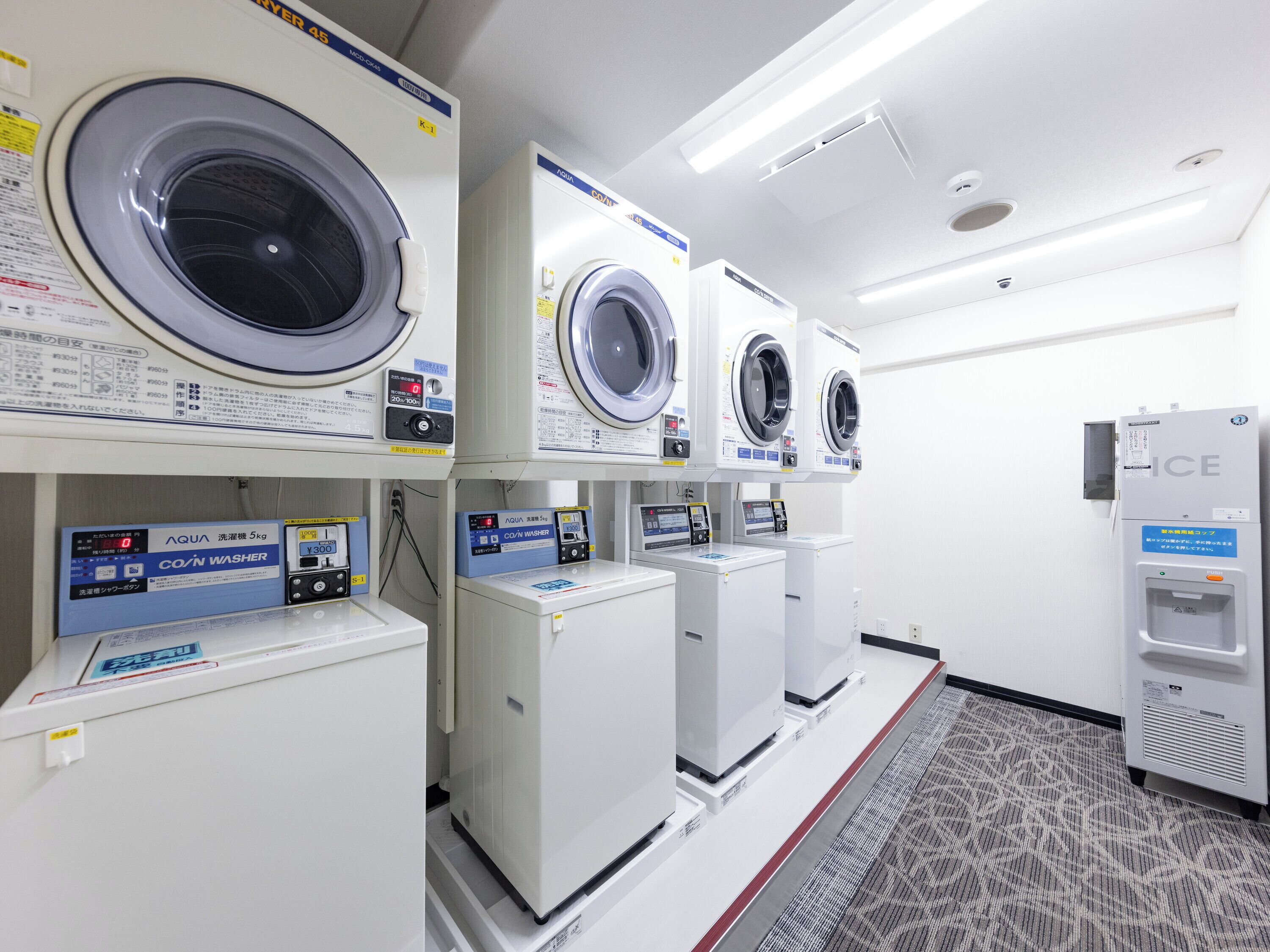 A laundry facility with multiple washing machines and dryers, including a COIN WASHER model.